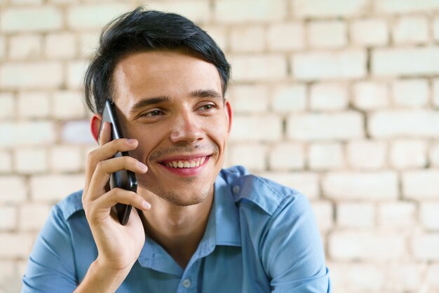 Happy teenager communicates on the phone closeup caucasian young brunette man on a background of a w...