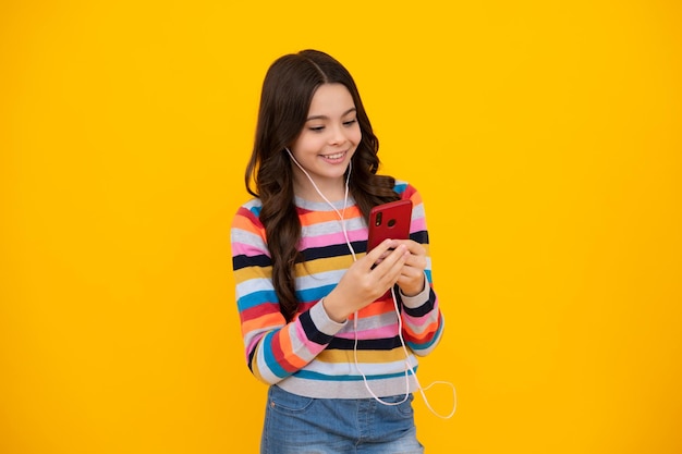 Happy teenager girl 12 13 14 years old with smart phone Hipster teen girl types message on cellphone enjoys mobile app Kid hold smartphone texting in online social media Internet addiction