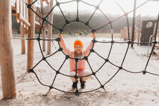 Happy teenager girl child playing in rope spider web at playground. children's sports.