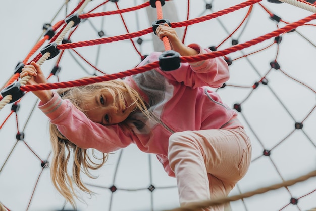 Happy teenager girl child playing in rope spider web at playground. children's sports.