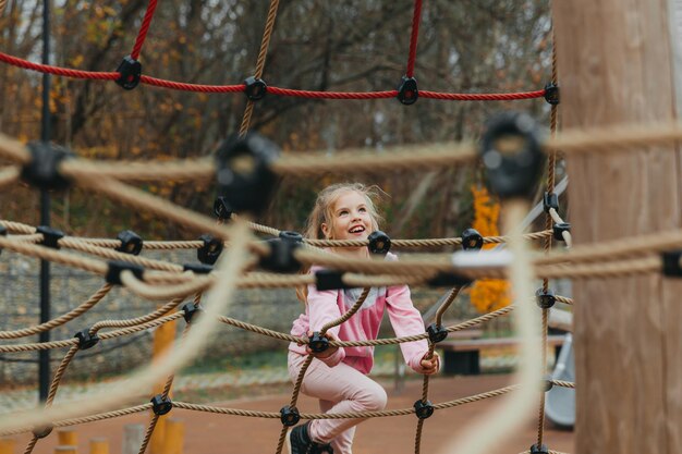 遊び場でロープクモの巣で遊んで幸せなティーンエイジャーの女の子の子供。子供のスポーツ。