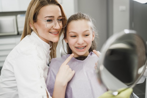 歯科医院での歯科治療後、鏡で歯を見ている幸せな10代の少女。