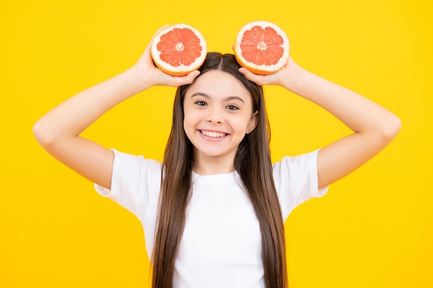 Tシャツを着た幸せな10代の女の子がグレープフルーツオレンジの子供たちの果物のビタミンを保持します