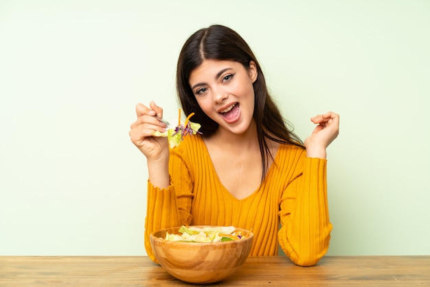 Ragazza felice dell'adolescente con insalata sopra la parete verde