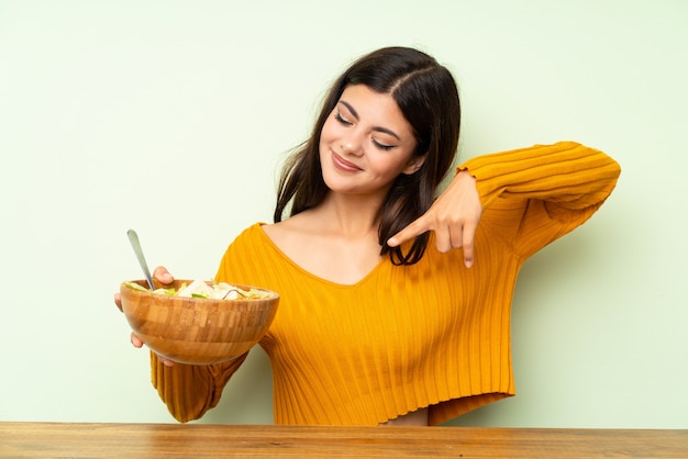 Happy Teenager girl with salad over green wall