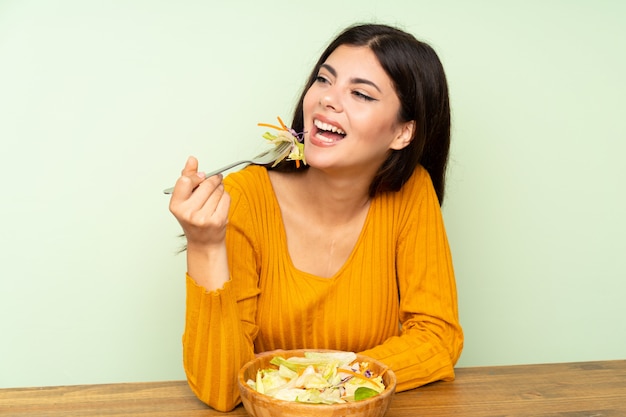 Happy Teenager girl with salad over green wall