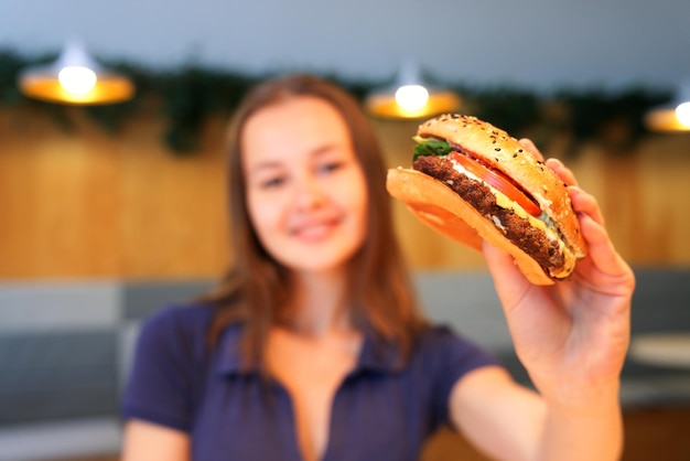 happy teenager girl young woman is holding big juicy fat burger hamburger Fast food restaurant