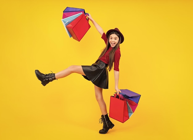 Happy teenager portrait Beautiful fashion teenager child girl with shopping bags yellow background