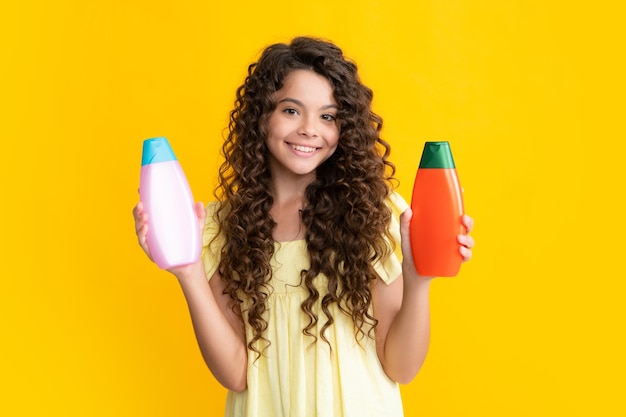 Happy teenager portrait of child girl with bottle shampoo\
conditioners or shower gel kids hair care hair cosmetic product\
shampoo bottle smiling girl