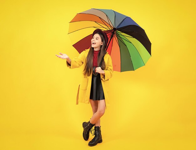 Happy teenager portrait happy teenager portrait teen girl under\
rainbow umbrella in autumn weather isolated on yellow background\
autumn kids clothes smiling girl in autumn coat