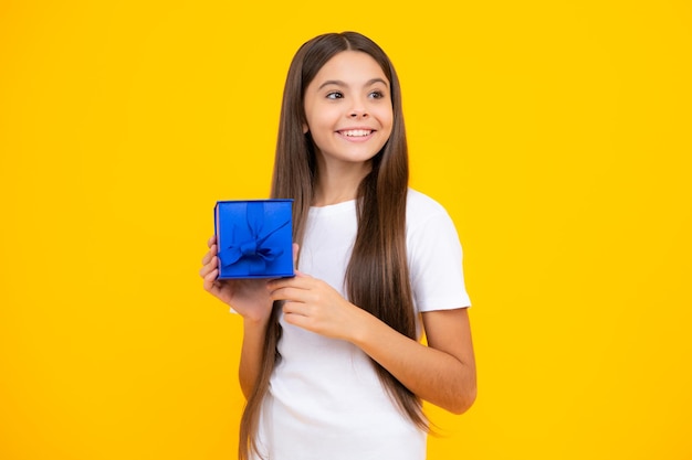 Happy teenager portrait Smiling girl in t shirt Teenager child holding gift box on yellow isolated background Gift for kids birthday Summer holiday