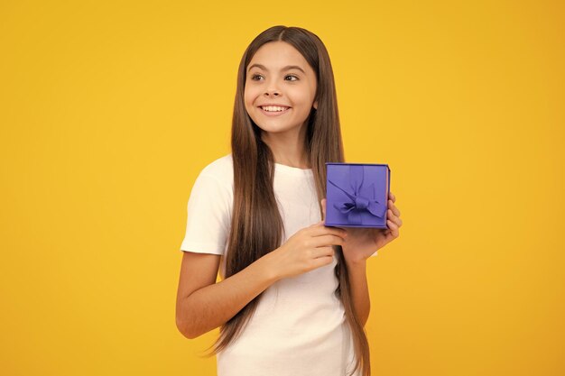 Happy teenager portrait smiling girl in t shirt teenager child\
holding gift box on yellow isolated background gift for kids\
birthday summer holiday