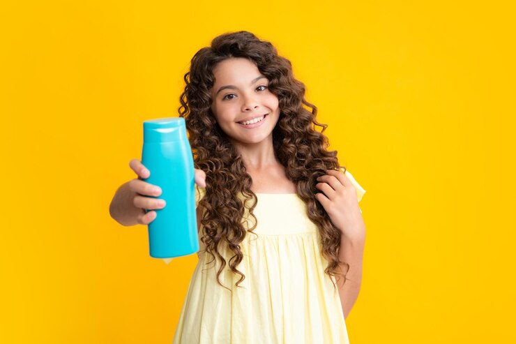 Happy teenager portrait Teen child girl with shampoo bottle or shower gel isolated on yellow background Kids hair cosmetic product Smiling girl