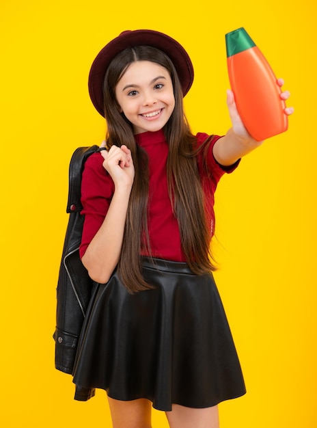 Happy teenager portrait Teen child girl with shampoo bottle or shower gel isolated on yellow background Kids hair cosmetic product Smiling girl