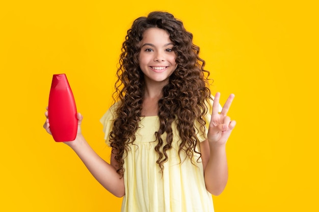 Happy teenager portrait teen child girl with shampoo bottle or shower gel isolated on yellow background kids hair cosmetic product smiling girl