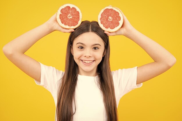 Happy teenager portrait Teenage girl holding a grapefruit on a yellow background Smiling girl