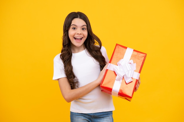 Happy teenager positive and smiling emotions of child girl Teenager kid with present box on isolated yellow background Teen girl giving birthday gift Present greeting and gifting concept