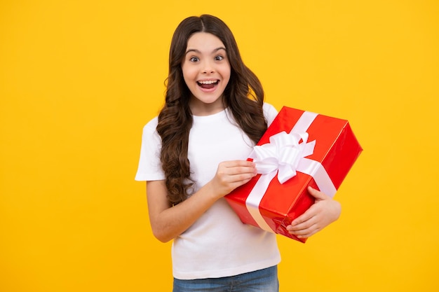 Happy teenager positive and smiling emotions of child girl Teenager kid with present box on isolated yellow background Teen girl giving birthday gift Present greeting and gifting concept