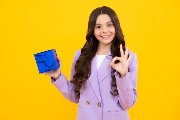 Happy teenager positive and smiling emotions of child girl Teenager kid with present box on isolated yellow background Teen girl giving birthday gift Present greeting and gifting concept