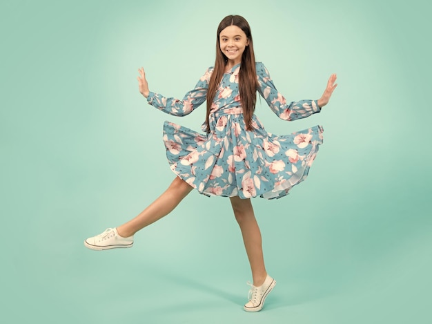 Happy teenager positive and smiling emotions Full length cheerful teenager kid jump enjoy rejoice win isolated on blue background Small child girl in summer dress jumping