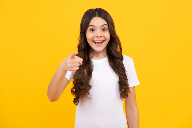 Happy teenager positive and smiling emotions of teen girl happy teenager positive and smiling emotions cheerful teen child posing isolated over yellow background pointing to you