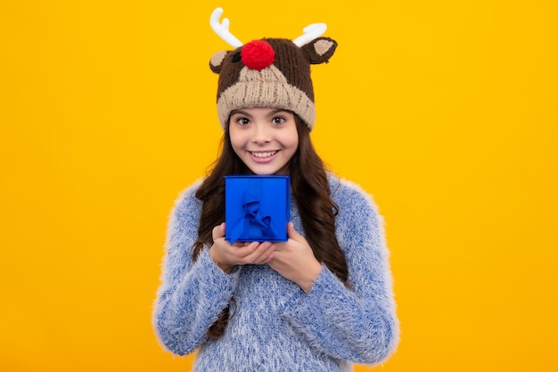 Happy teenager positive and smiling emotions of teen girl
teenager child in funny winter hat holding gift box on yellow
isolated background gift for kids birthday christmas or new
year