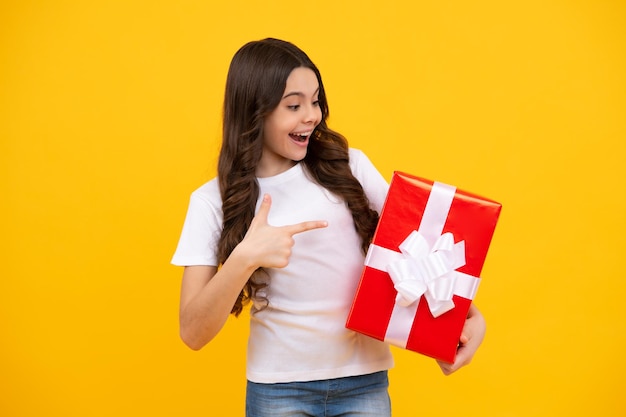 Happy teenager positive and smiling emotions of teen girl\
teenager child in t shirt holding gift box on yellow isolated\
background gift for kids birthday summer holiday