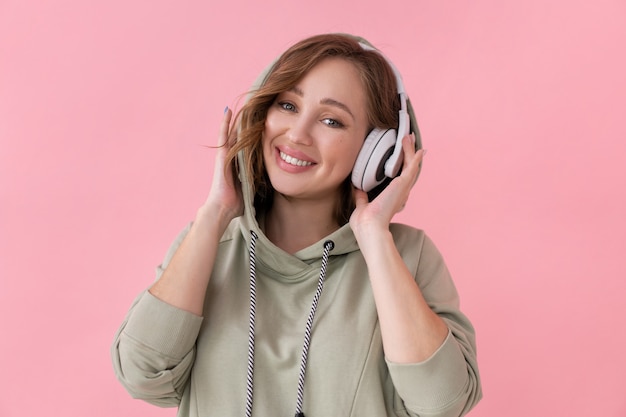 Happy teeth smile woman listen music headphones Caucasian female enjoy podcast or audio books dressed oversize hoodie pink background close up portrait