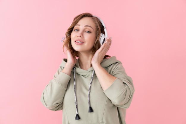 Denti felici sorridere donna ascoltare musica cuffie femmina caucasica godere di podcast o libri audio vestito oversize felpa con cappuccio sfondo rosa primo piano ritratto