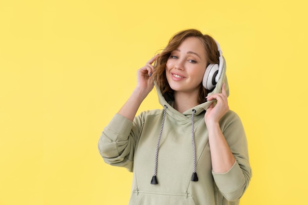 Happy teeth smile woman listen music headphones Caucasian female enjoy podcast or audio books dressed oversize hoodie yellow background close up portrait