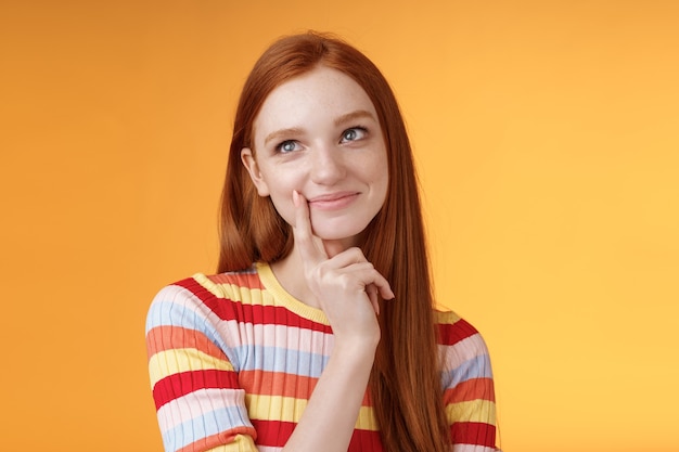 Happy tender feminine redhead 20s girl university student smiling delighted dreaming tasty slice pizza touching lip thoughtful, thinking daydreaming look upper left corner imaging desires.