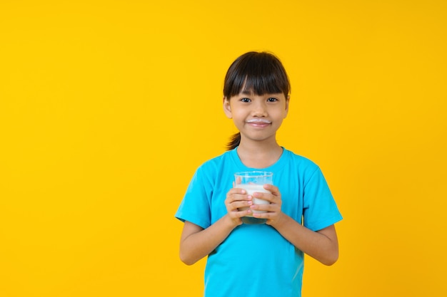 Happy Thai kid holding glass of milk isolated, young Asian girl drinking milk