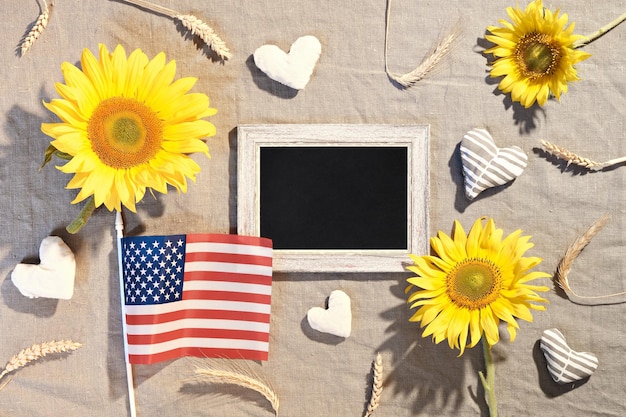 Happy thanksgiving-tekst op blackboard. vlag van de vs, zonnebloemen, herfstversieringen. plat op beige textiel met tarweoren, seizoensbloemen, gevulde katoenen harten. amerikaans herfst oogstfeest.