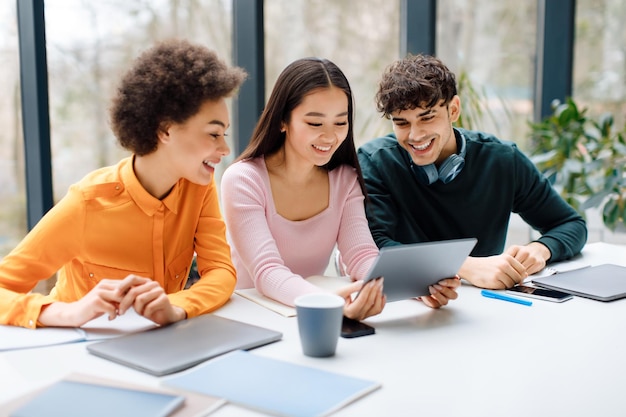 3人の幸せな国際学生が ディジタルタブレットを使って 議論しています