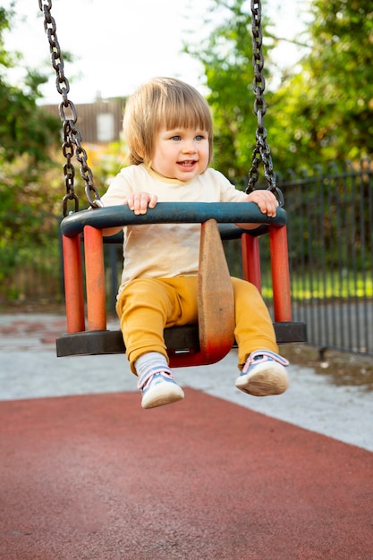 Happy toddler, baby or child on playground area. Playingat swing. Education, parenting, active games outside.