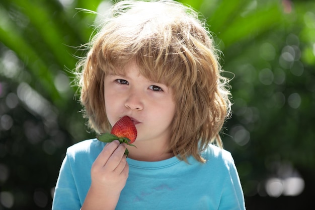 Happy toddler boy with fresh strawberries on green summer background