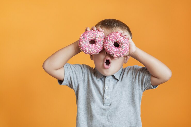彼の目の近くに2つのドーナツを持つ幸せな幼児の男の子