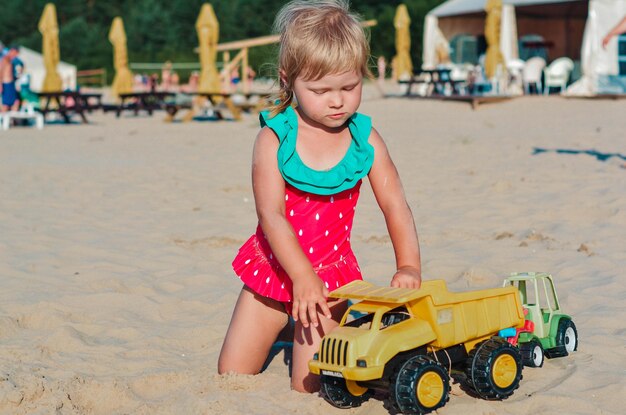 Foto bambino felice che gioca sulla spiaggia con una macchina giocattolo