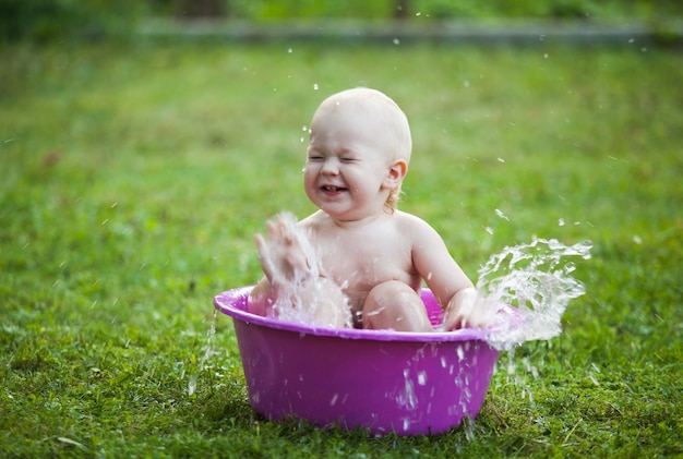 庭の芝生の上の洗面器で幸せな幼児