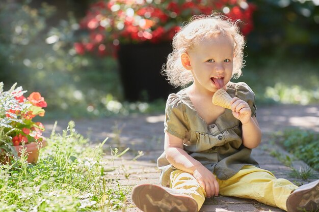 Счастливый малыш с мороженым сидит на траве в лучах солнца