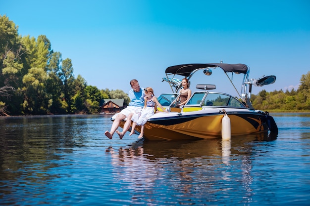 Happy together. Caring young father and his little daughter sitting on the bow of the boat together while the mother observing them fondly