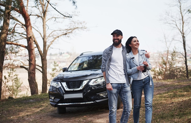 Happy together. Embracing and enjoying the nature. Couple have arrived to the forest on their brand new black car