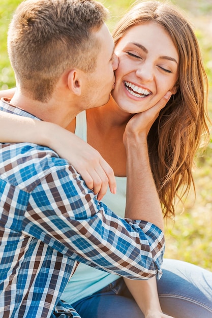 Happy together. Young man kissing beautiful cheerful women while she hugging him and looking at the camera.