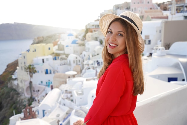 Happy tourist girl enjoying travel in Greece Beautiful woman smiling and looking at camera visiting on sunset Oia village in Santorini island Greece Europe