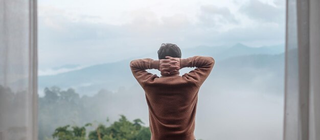 아침에 시골집이나 홈스테이에서 휴식을 취하고 산 전망을 바라보는 행복한 관광 남자. 휴가, 블로거, SoloTravel, 여행, 여행 및 편안한 개념