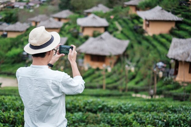 美しい茶園で携帯スマートフォンで写真を撮る白いシャツを着た幸せな観光客の男。