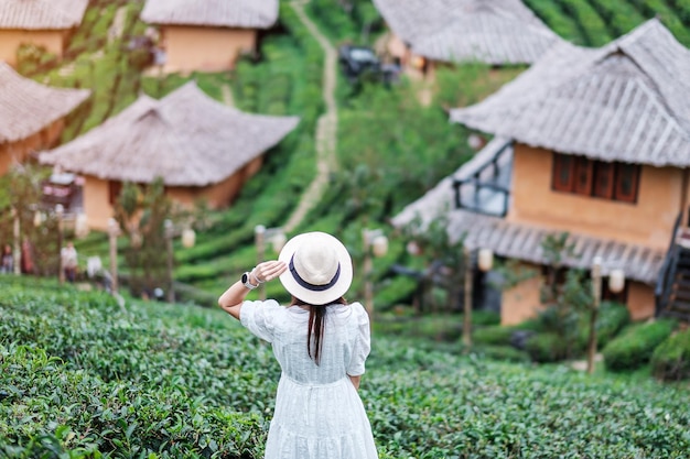 Happy tourist woman in white dress enjoy beautiful tea\
gardentraveler visiting in ban rak thai village mae hong son\
thailand travel vacation and holiday concept