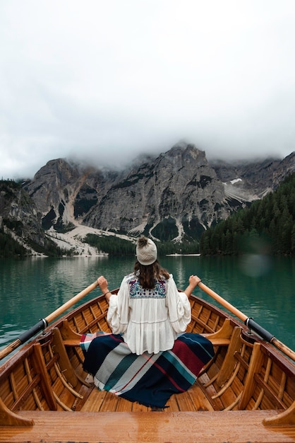 이탈리아 알프스의 산으로 둘러싸인 Braies 호수에 나무 보트에 앉아 모자와 함께 행복 관광 여자