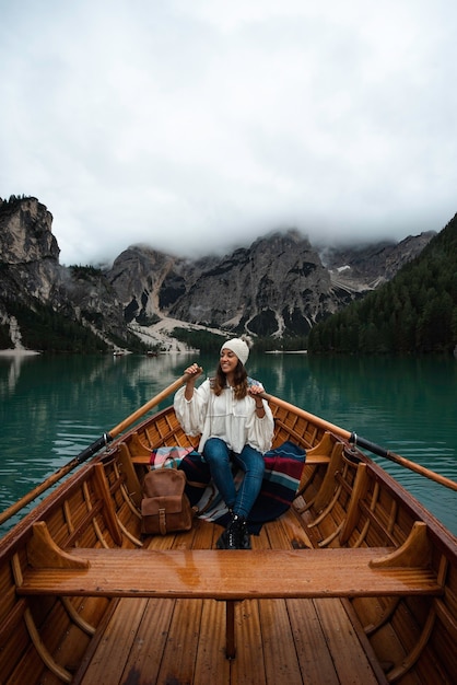 Happy tourist woman with hat sitting in a wooden boat on Braies lake surrounded by the mountains of the Italian Alps