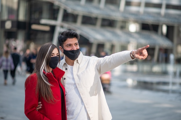 covid 또는 코로나바이러스 마스크를 쓴 행복한 관광객 커플이 도시를 걷고 흥미로운 장소를 가리키고 있습니다